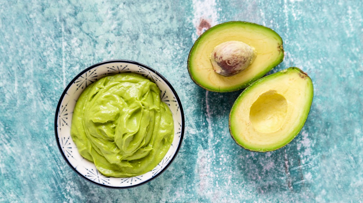 Se abre un aguacate para revelar la pulpa del interior, con un tazón de guacamole junto con el aguacate fresco.